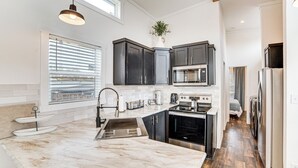A modern kitchen with dark cabinets, a large island, and a view through the window.