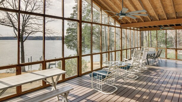 En inglasad veranda med trägolv, stora fönster och utomhusmöbler.