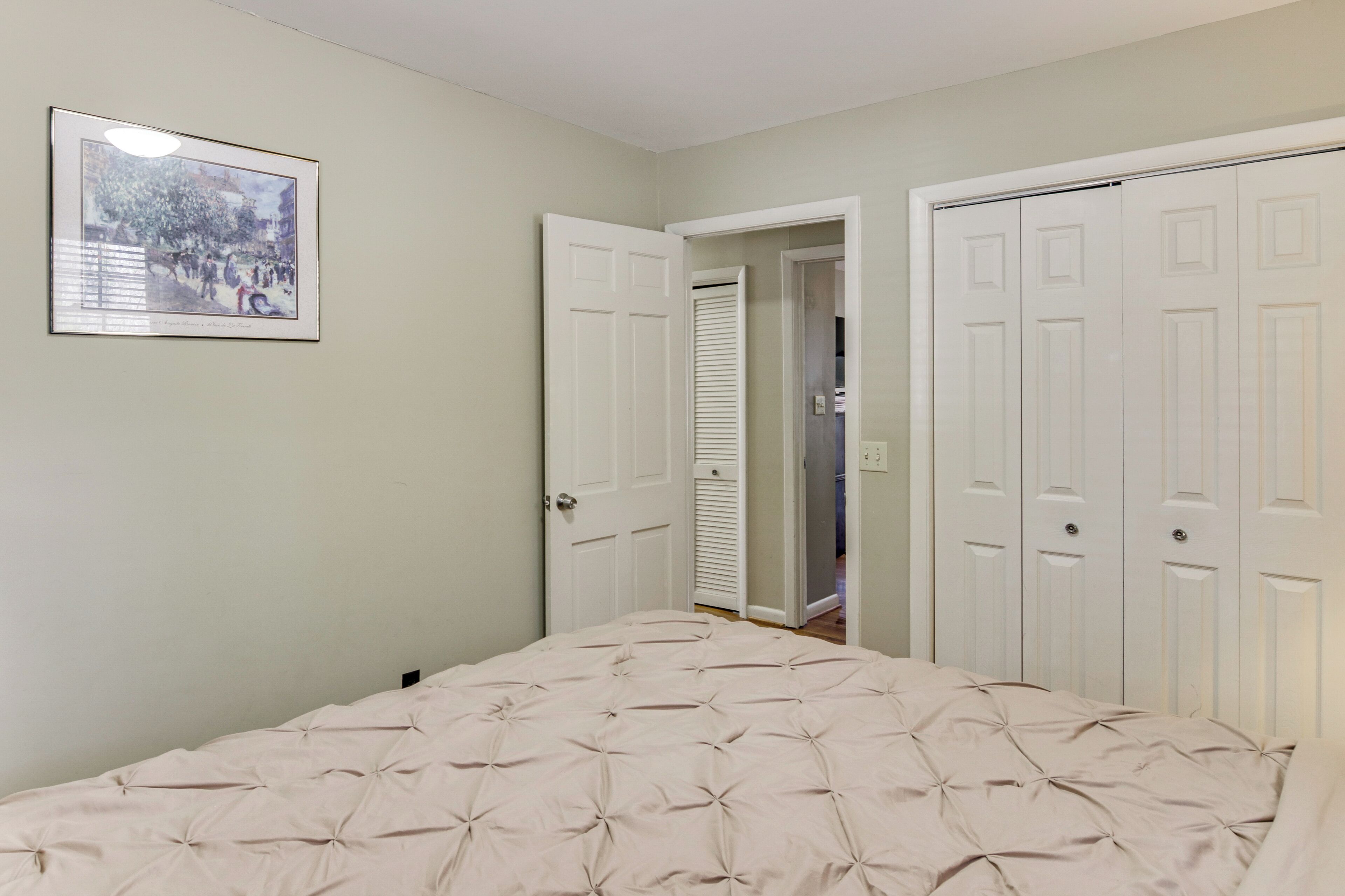 Een slaapkamer met een bed, een deur en een ingelijst kunstwerk aan de muur.
