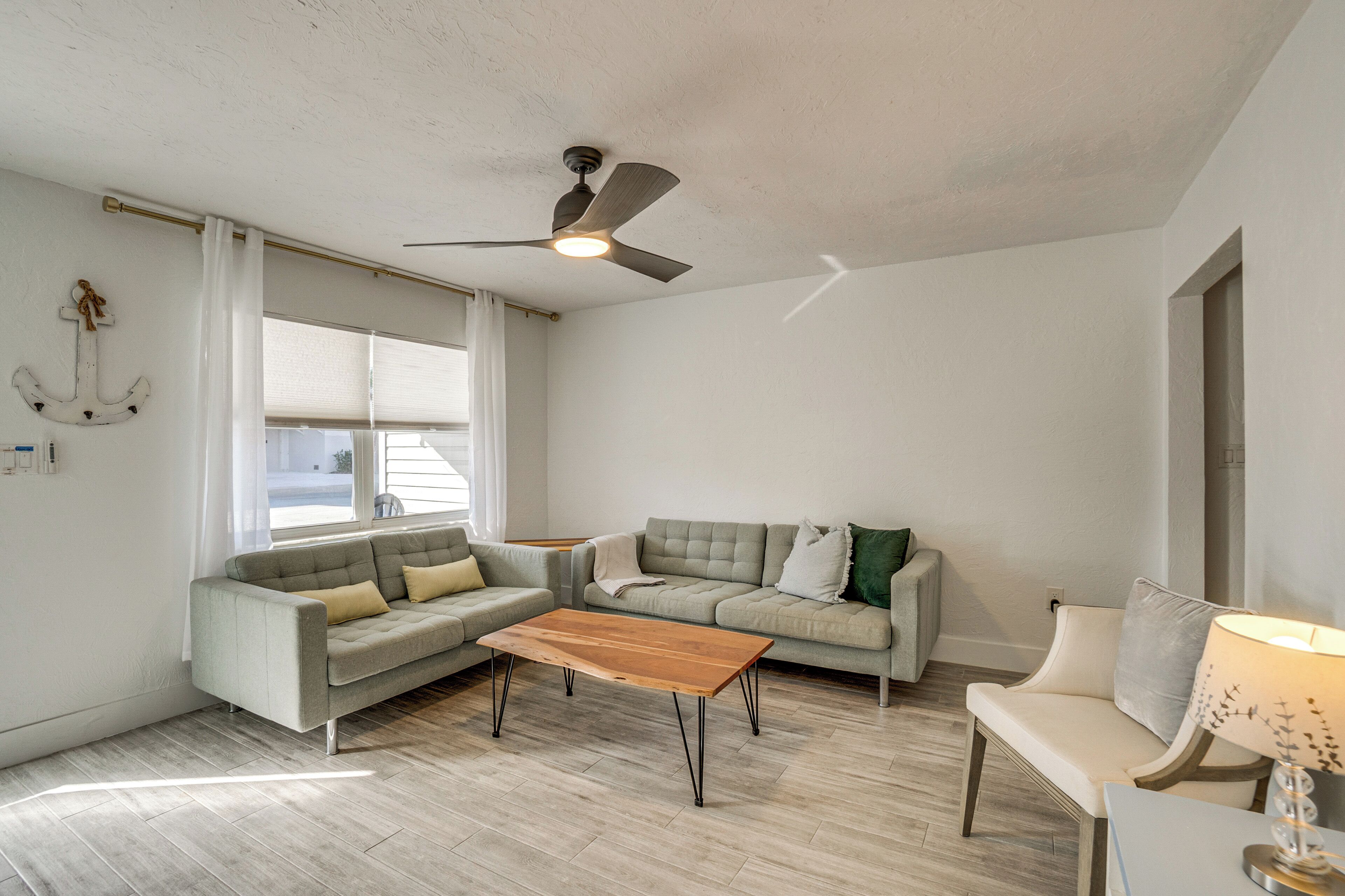 Ein geräumiges Wohnzimmer mit Deckenventilator, zwei grauen Sofas, einem Holztisch und einer Lampe.