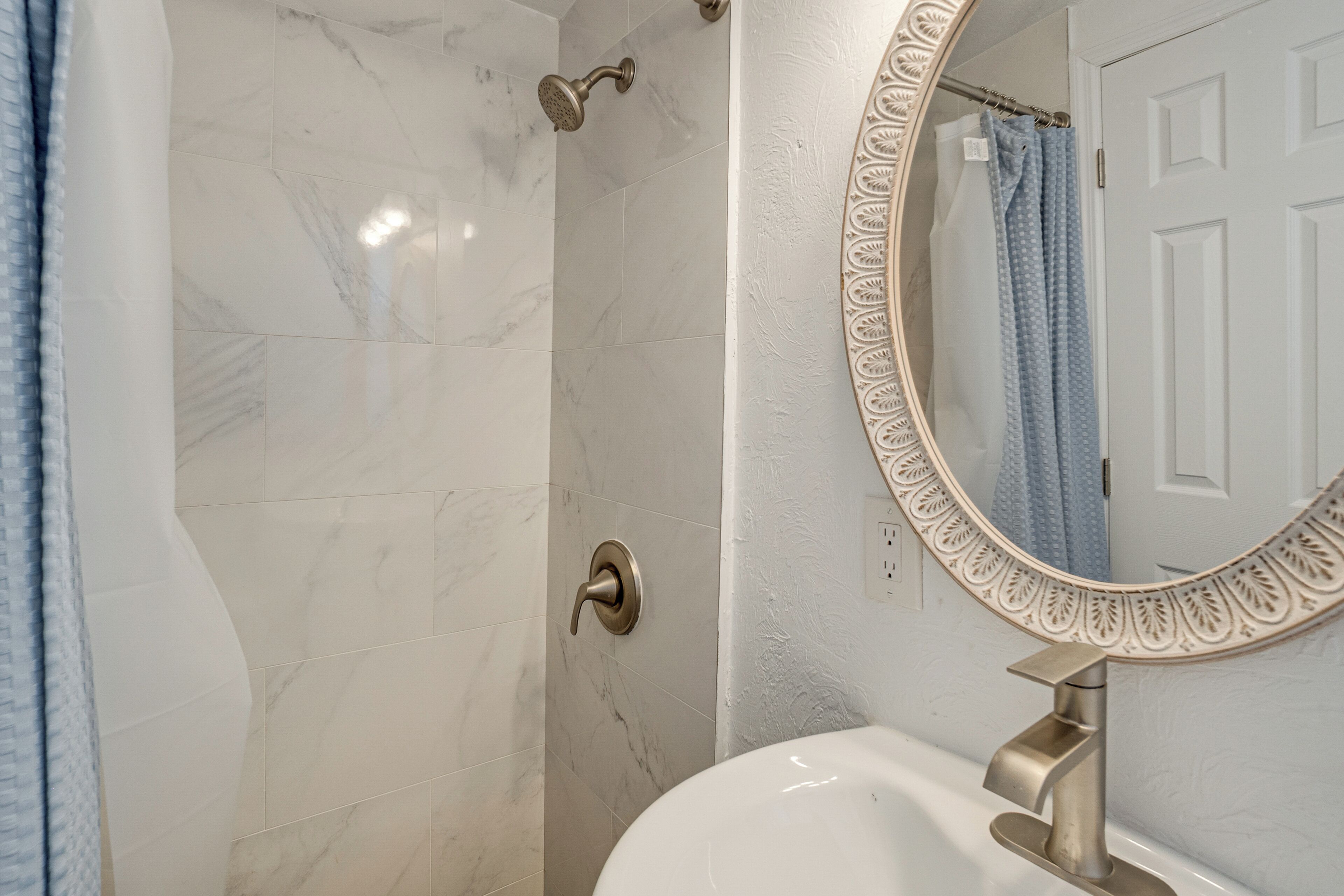 Een badkamer met een witte marmeren douche, een wastafel met een moderne kraan en een decoratieve spiegel met een sierlijk frame.