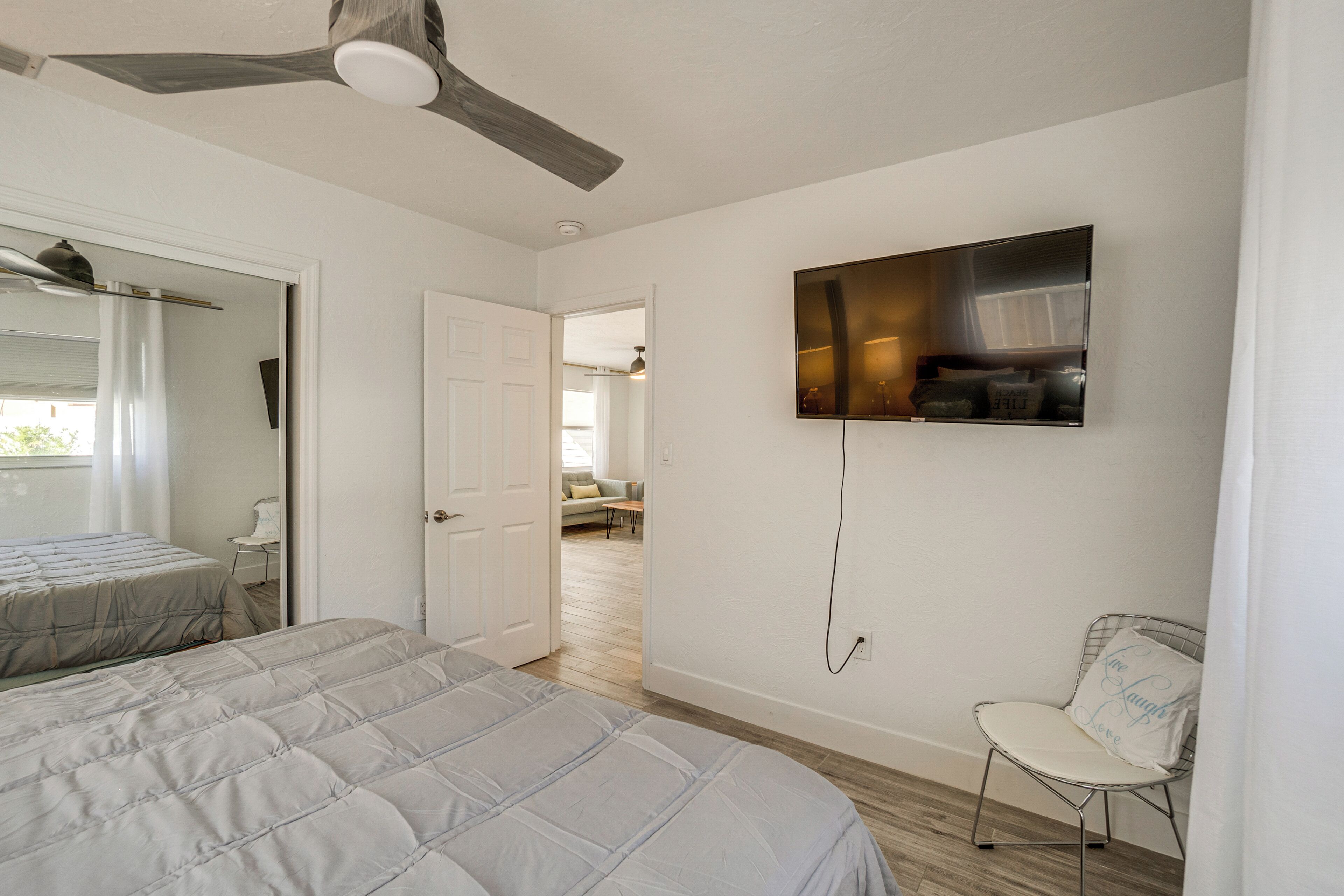 A bedroom with a bed, a chair, a ceiling fan, and a TV mounted on the wall.