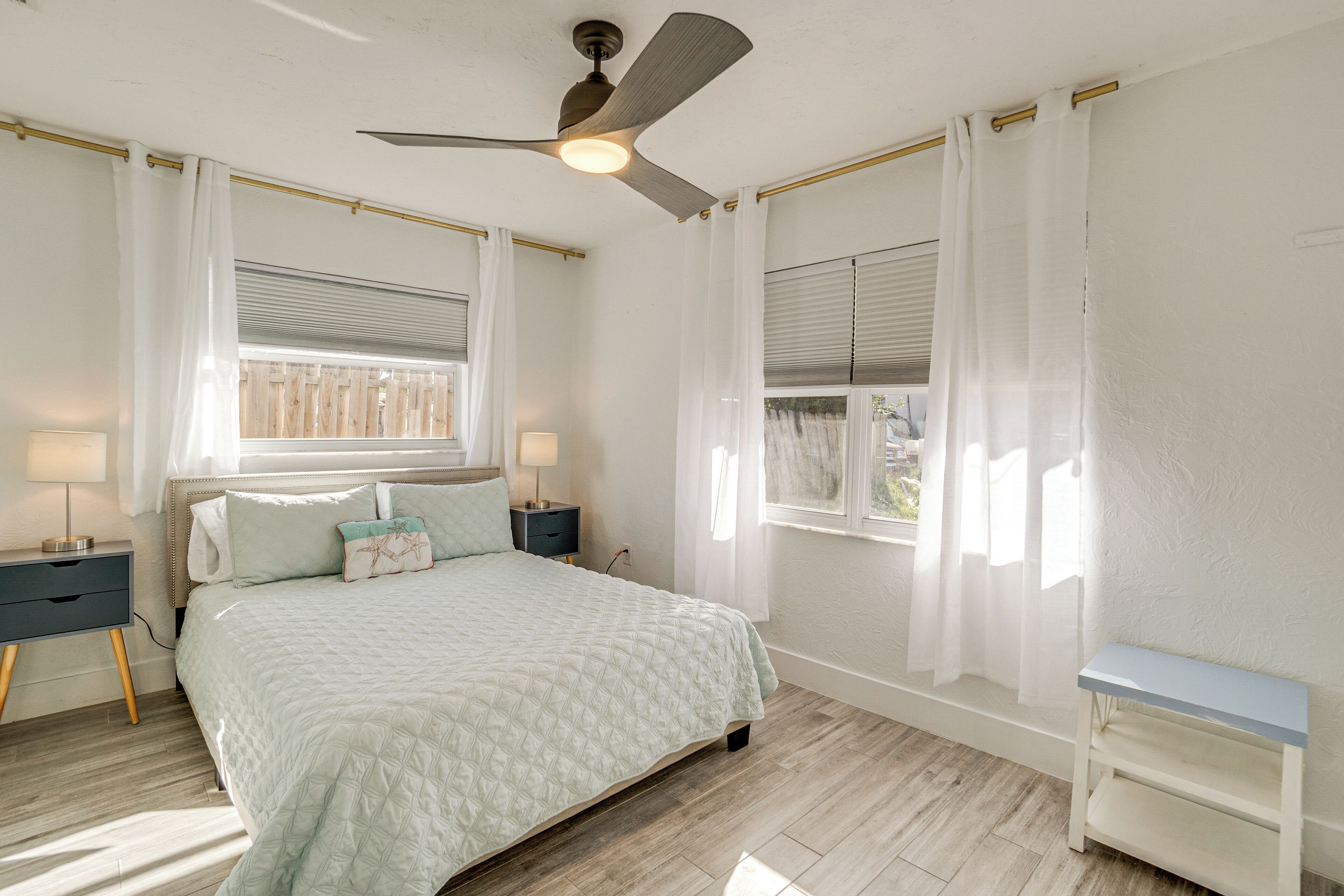 A bedroom with a bed, bedside tables, a ceiling fan, and a window with curtains.