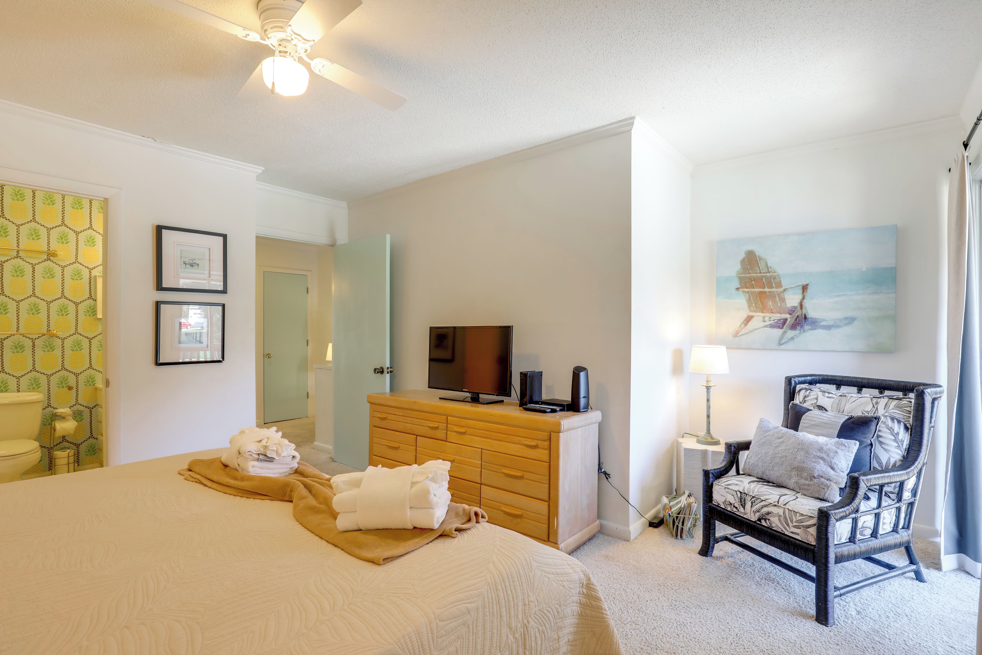 A hotel room with a bed, a wooden dresser, a chair, a television, and artwork on the walls.