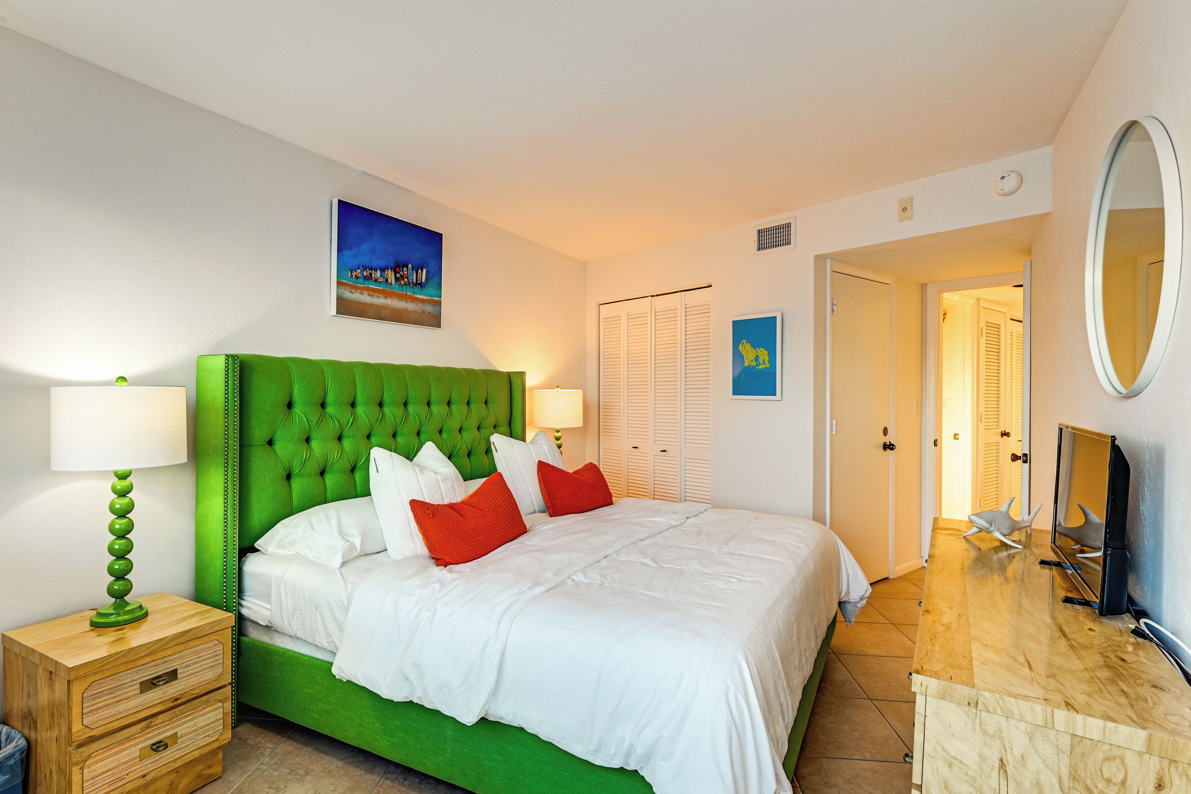 A bedroom with a green upholstered headboard, white bedding, and a wooden nightstand with a lamp.