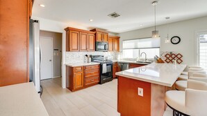A modern kitchen with wooden cabinets, a stainless steel refrigerator, a microwave, an oven, and a large island with bar stools. - Pool + Putting Green: Quiet Scottsdale Oasis! (Scottsdale)