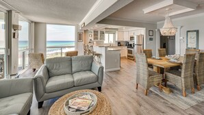 A spacious living area with a grey sofa, wicker chairs, and a wooden dining table. - Steps to Beach: Oceanfront w/ Panoramic Gulf Views (Destin)