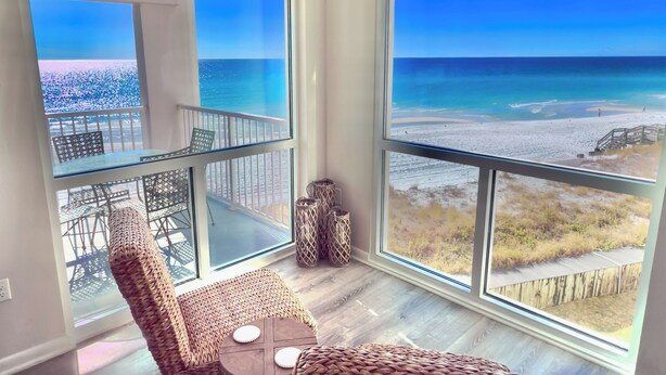 A balcony with wicker furniture, large windows with ocean views, and a wooden floor. - Steps to Beach: Oceanfront w/ Panoramic Gulf Views (Destin)