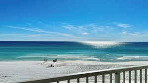 A beach with a clear sky, calm sea, and a white railing in the foreground. - Steps to Beach: Oceanfront w/ Panoramic Gulf Views (Destin)