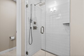 Una cabina doccia in vetro con soffione a mano, pannello comandi a parete e porta carta igienica.