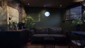 Una habitación acogedora con pared verde oscuro, un ventanal redondo, un sofá de cuero negro, una mesita pequeña y una planta en maceta.