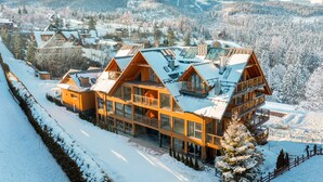 Eine große Holzhütte mit mehreren Balkonen und großen Fenstern, umgeben von schneebedeckten Bergen.