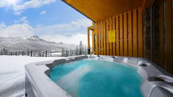 Un jacuzzi con terraza de madera y vista a montañas nevadas.