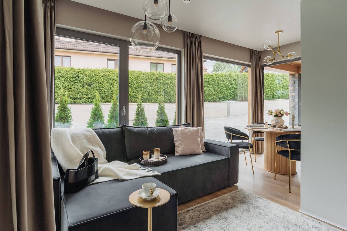 Una sala de estar moderna con un sofá gris oscuro, una mesita redonda pequeña y una zona de comedor con una mesa de madera y sillas.