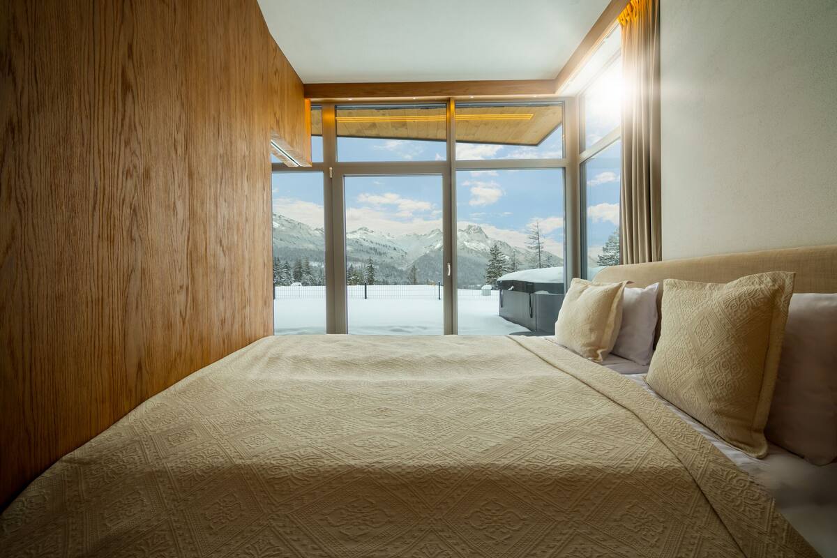 Un dormitorio con una cama grande, cabecera de madera y vistas a montañas nevadas a través de una puerta de cristal.
