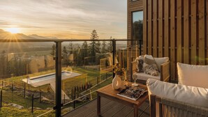 Ein Balkon mit einem Holztisch, einer weißen Vase mit Blumen und einer Couch mit Kissen.