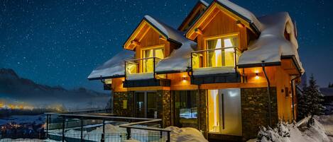 A wooden chalet with a balcony and a stone facade, surrounded by snow.
