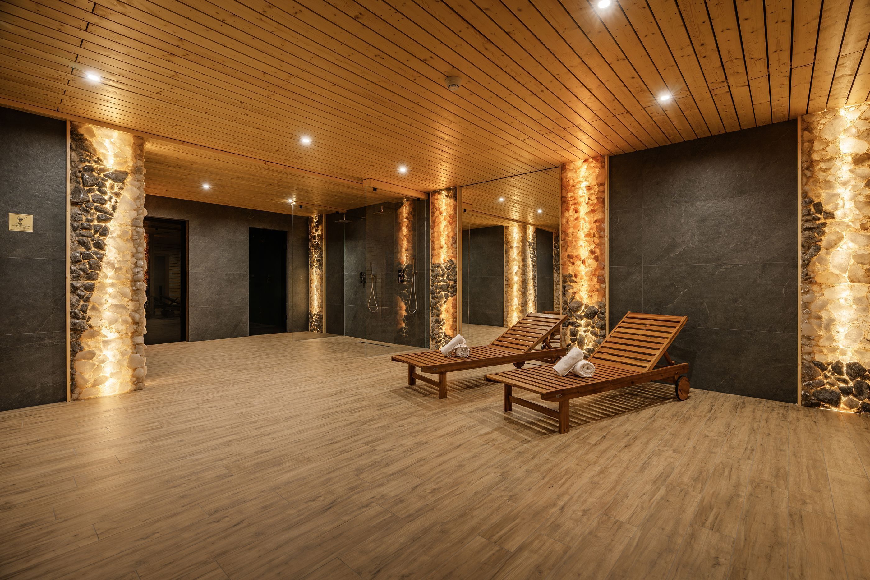 A spa room with wooden flooring, stone pillars, and wooden loungers.