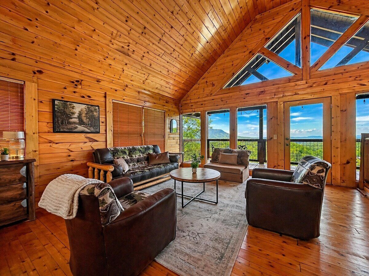 A spacious room with a high wooden ceiling, large windows, a sofa set, and a round coffee table.