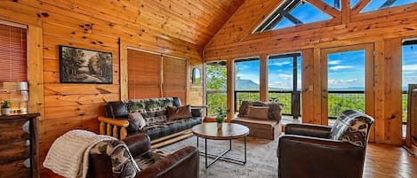 A spacious room with a high wooden ceiling, large windows, a sofa set, and a round coffee table.