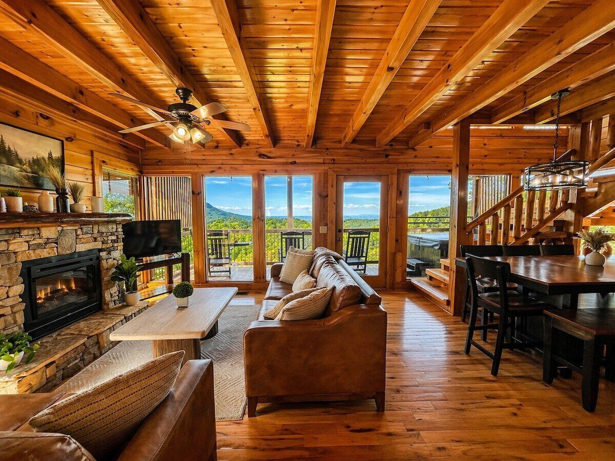 A spacious living area with a stone fireplace, leather sofa, wooden dining table, and a television.