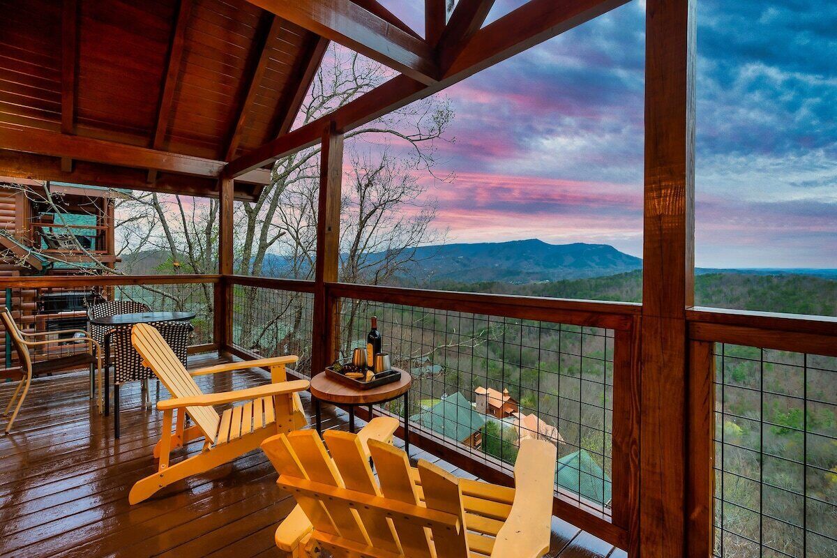 Une terrasse en bois, agrémentée de chaises Adirondack et d’une table, offrant une vue sur un paysage montagneux.