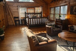 A cozy cabin interior with a wooden floor, a bed with a wooden headboard, a sofa, a chair, and a small table. - Eagle Cloud Escape- Amazing Views -Hot Tub -Game Room -Arcade -Pool -& MORE (Sevierville)