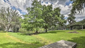 Een gazon met een houten steiger, bomen en een overdekte constructie nabij water.