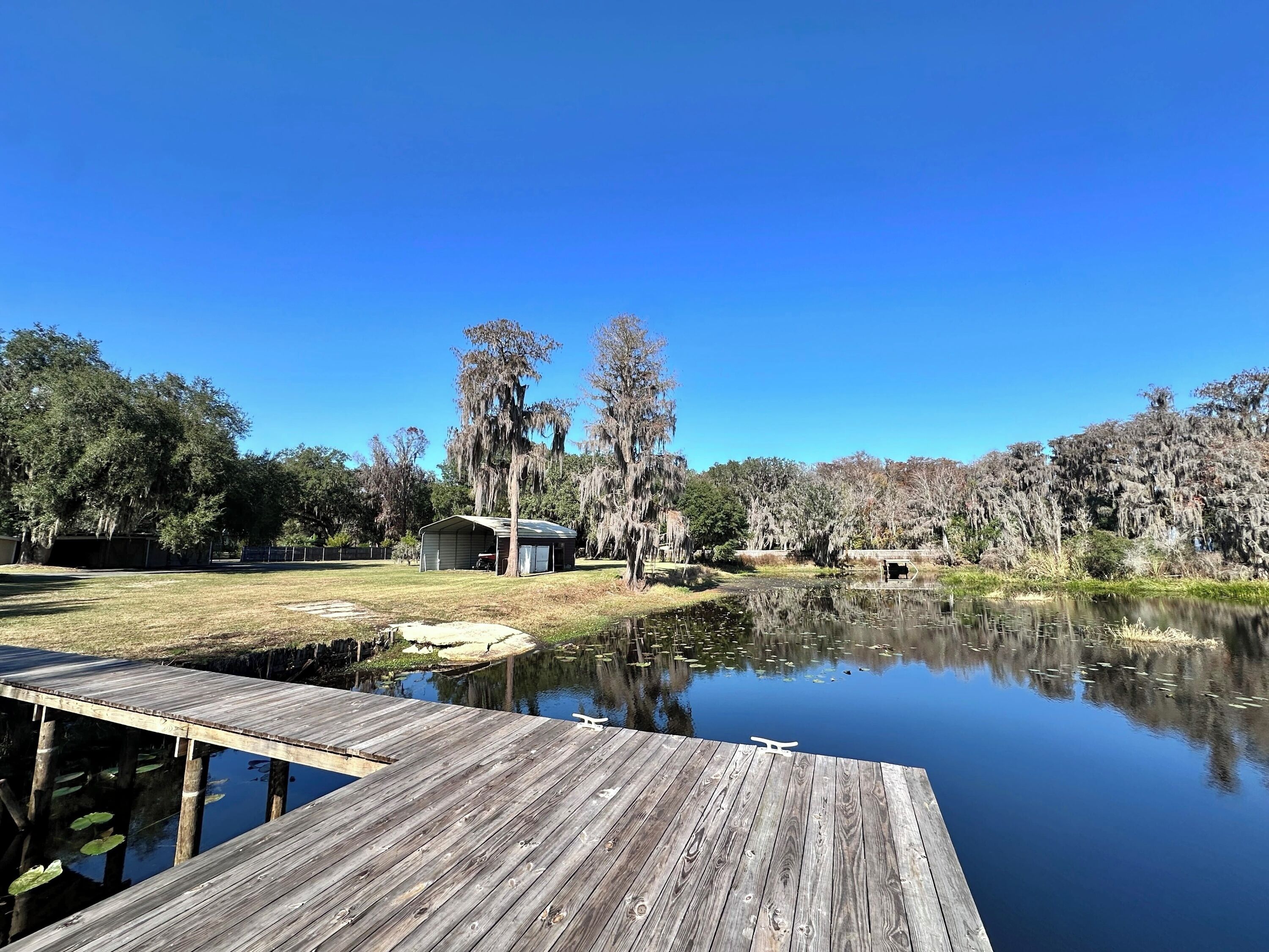 A wooden dock extending over a calm lake, surrounded by trees and a small building.