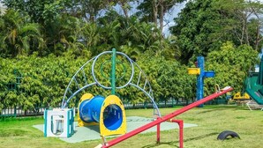Un parque infantil con un balancín, un tobogán azul y amarillo y una estructura para escalar.
