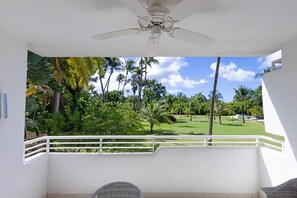 A balcony with a ceiling fan, white railings, and a view of a golf course with palm trees. - Glitter Bay Estate 214 1 Bedroom Apts (Holetown)