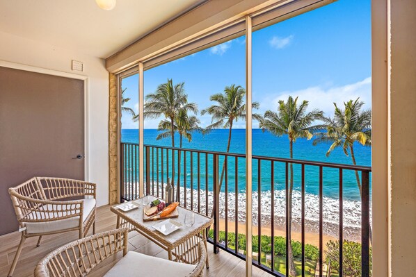Un balcon agrémenté de meubles en osier, une table avec de la nourriture et des boissons, et une vue sur la plage et l’océan.