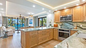 A modern kitchen with wooden cabinets, a marble countertop, and stainless steel appliances. - Where Sky Meets Sea Kihei Rooftop Corner Retreat Expansive Lanai and Views (Kihei)