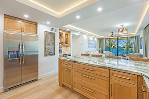 Una cocina moderna con un refrigerador de acero inoxidable, armarios de madera y encimera de mármol.
