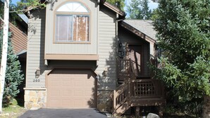 A two-story house with a brown garage door, a stone foundation, and a wooden deck. - Beautifully Remodeled Townhome on Peak 8 (Breckenridge)