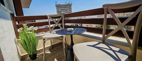 A balcony with a table and chairs, a potted plant, and a view of a building in the background.
