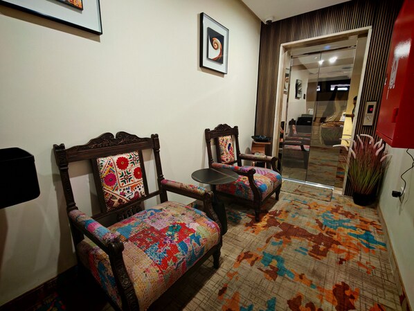 A room with two wooden chairs with colorful upholstery, a small round table, a patterned rug, and a framed picture on the wall. - Friends Hotel Jordan (Amman)