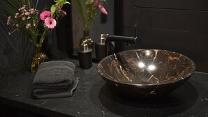 Et badeværelse med en sort marmorvask, et håndklæde og to vaser med lyserøde blomster.
