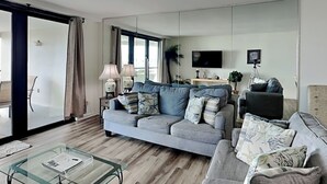 A modern living room with a grey sofa, a glass coffee table, and a TV mounted on the wall. - Edgewater #1101 | Gulf Front + Resort Amenities (Miramar Beach)