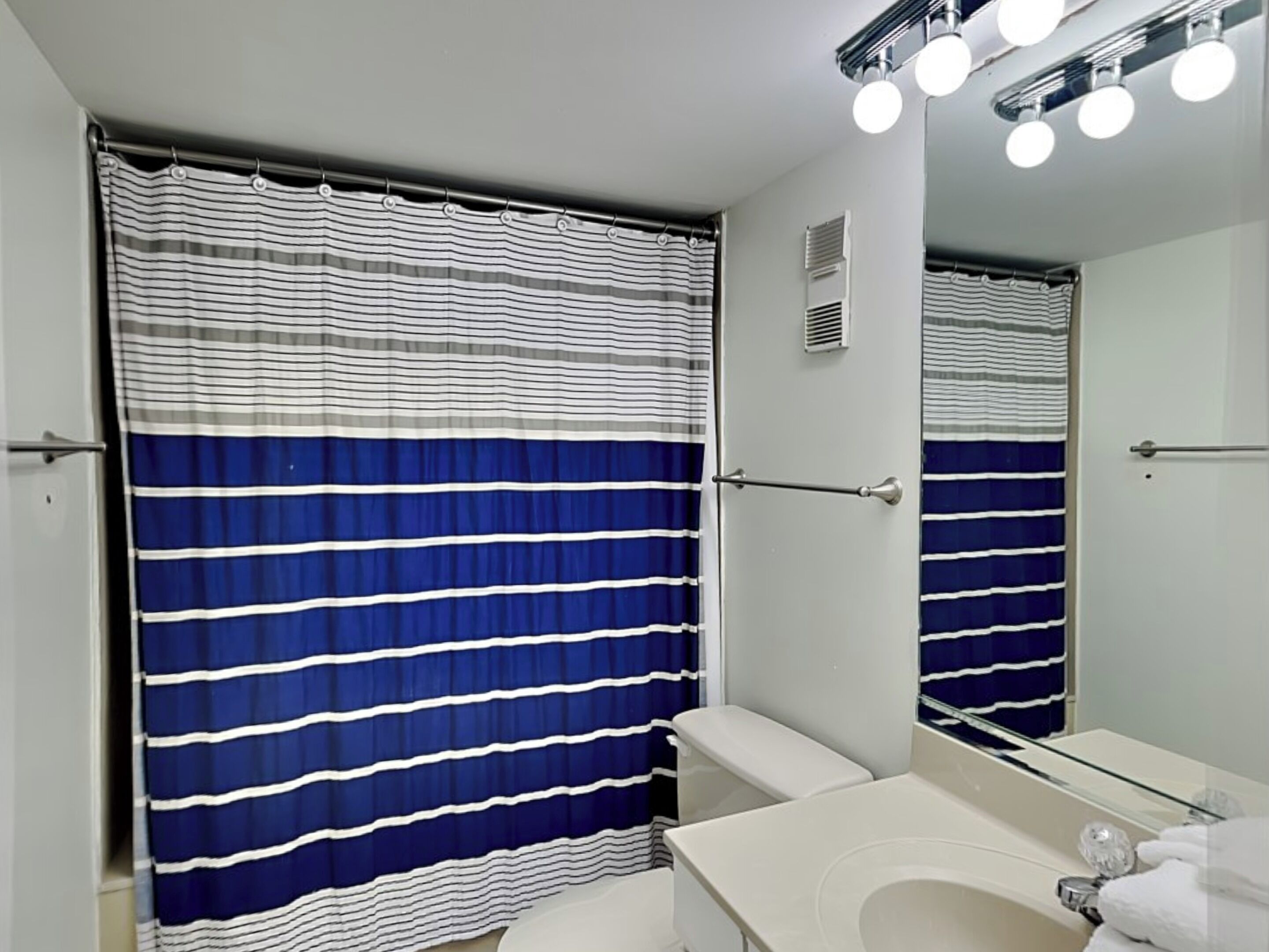 A bathroom with a striped shower curtain, a toilet, a sink with a mirror, and a towel rack.