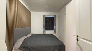 A bedroom with a bed, a window with curtains, a wooden panel wall, and a door. - Apartment in the heart of Esbjerg Center (Esbjerg)