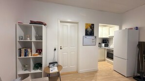 A compact kitchen with white cabinets, a microwave, and a refrigerator. A wooden door leads to a living area with a bookshelf and a small table. - Apartment in the heart of Esbjerg Center (Esbjerg)