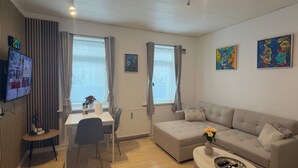 A modern living room with a sofa, a dining table, and a TV mounted on the wall. - Apartment in the heart of Esbjerg Center (Esbjerg)