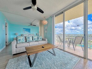 A living room with a sofa, a coffee table, a ceiling fan, and a view of a balcony with chairs. - Estero Beach & Tennis Club #801C Beachfront Condo (Fort Myers Beach)
