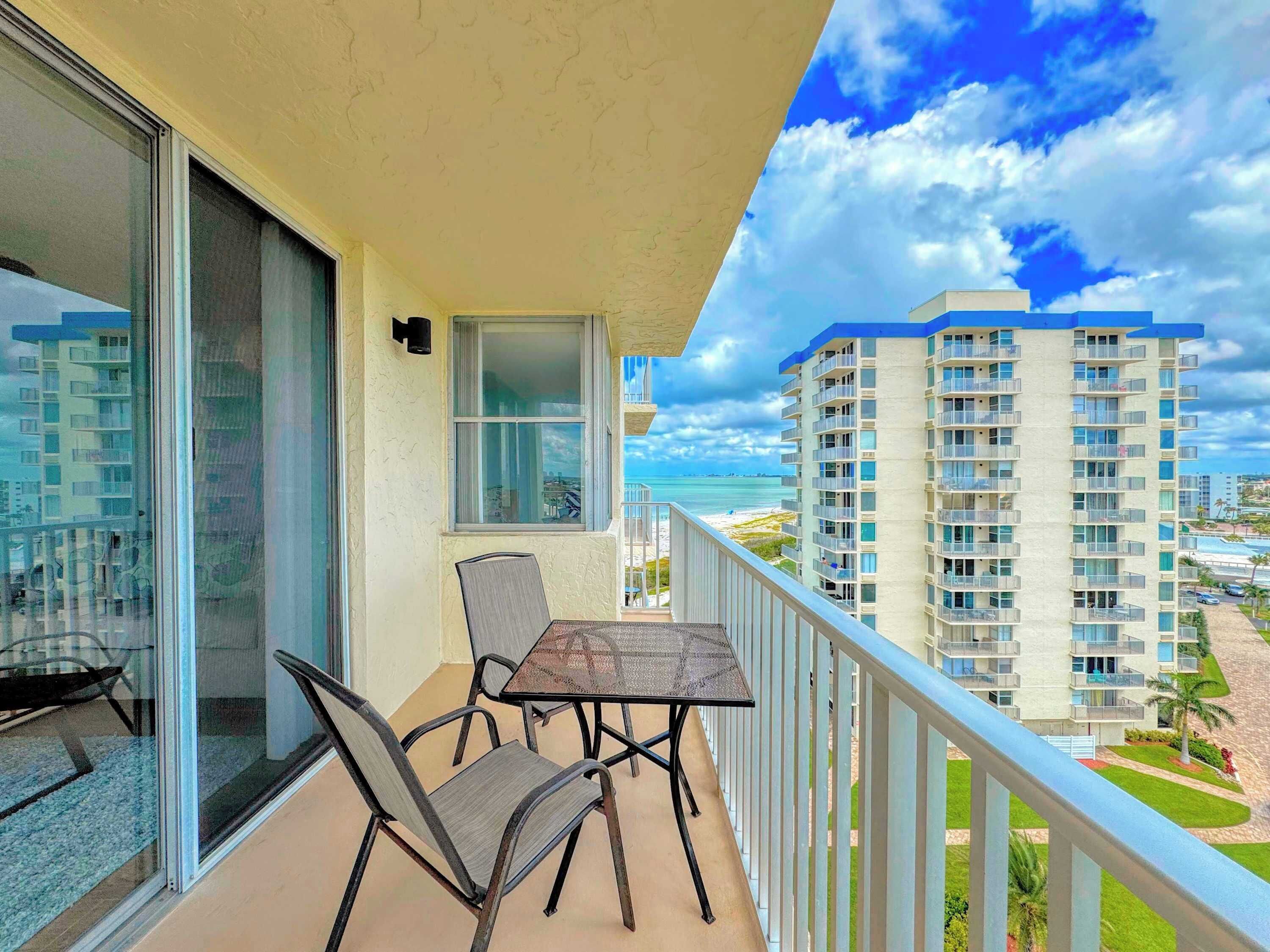 A balcony with a table and chairs, overlooking a beach and high-rise buildings.