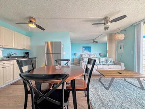 A modern kitchen with a stainless steel refrigerator, a dining table with chairs, and a living area with a sofa and a hanging light fixture. - Estero Beach & Tennis Club #801C Beachfront Condo (Fort Myers Beach)
