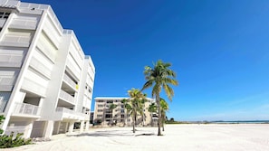 Een strandhotel met meerdere balkons, palmbomen en een helderblauwe lucht.