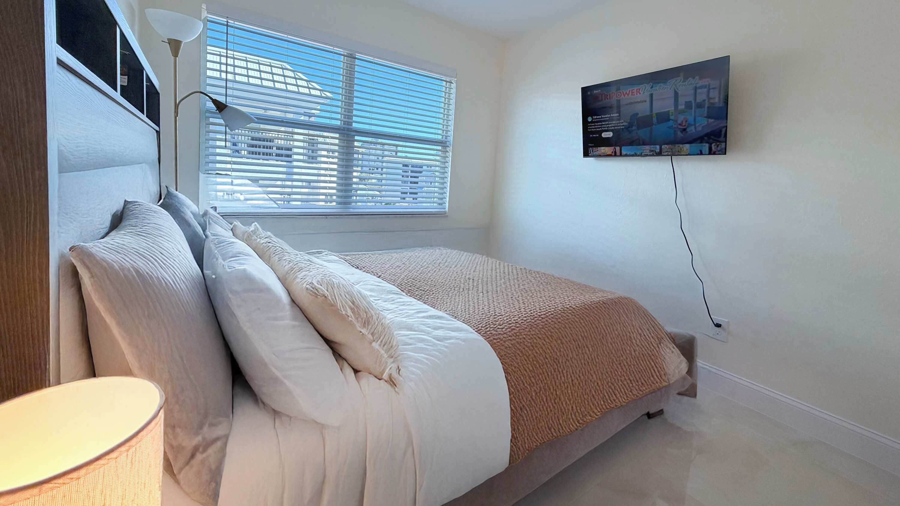 Ein Schlafzimmer mit einem Bett, einer Lampe, einem Fernseher und einem Fenster mit Jalousien.