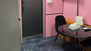 A conference room with a clock, a refrigerator, a table with a tissue box, a chair, and a wall-mounted light fixture. - Seafront Studio C4 (Simpson Bay)
