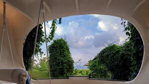 Una habitación con un amplio ventanal ovalado, una hamaca y vistas a zonas verdes y un edificio.